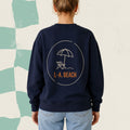 Dos d'un chandail crewneck bleu marine avec parasol et chaise longue illustres et le logo L.-A. Beach, boutique Sans Filtre