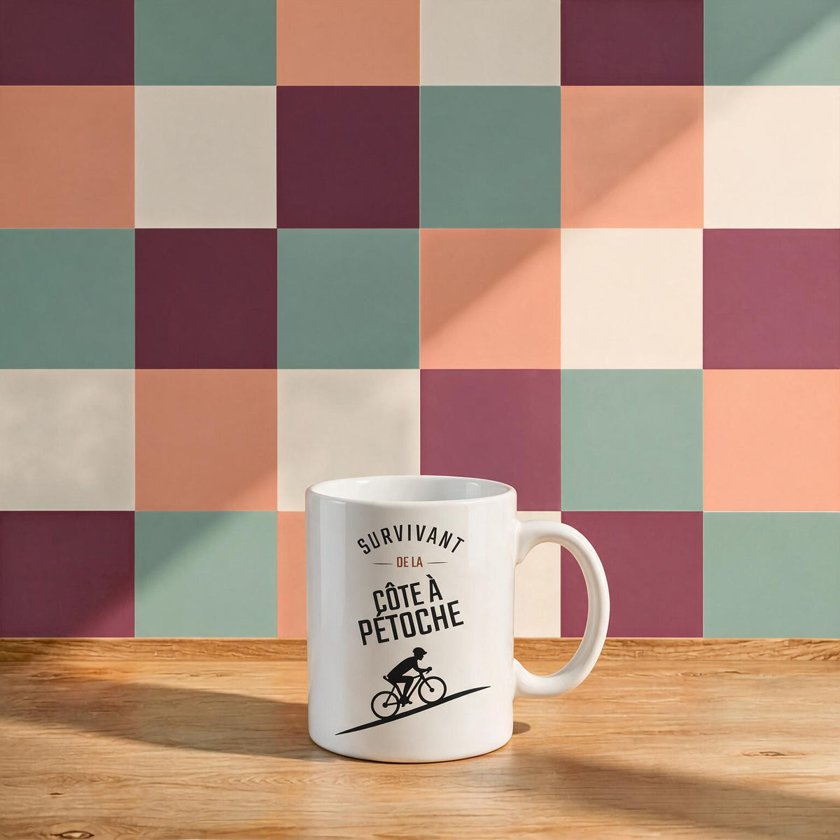 Tasse blanche avec cycliste illustre et le message Survivant de la cote a Petoche, posee sur une table en bois, boutique Sans Filtre
