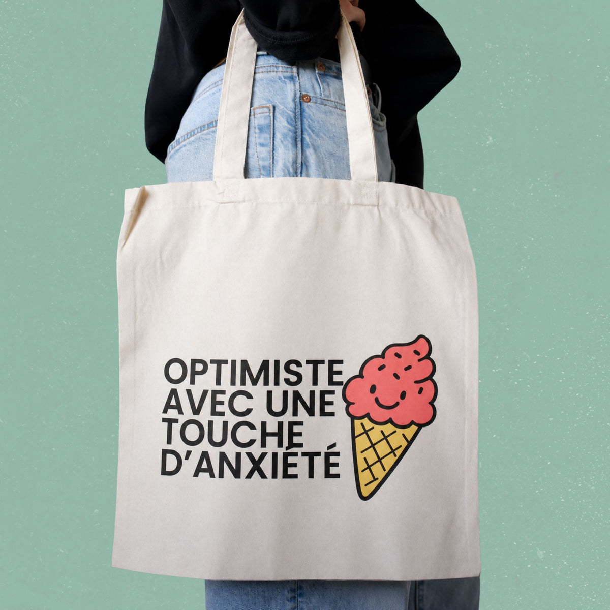 Sac fourre-tout ecru avec cornet de creme glacee illustre et le message Optimiste avec une touche d'anxiete, boutique Sans Filtre